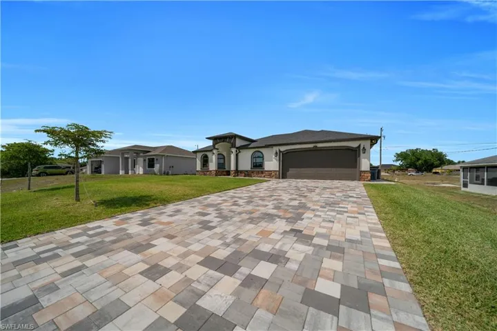 View of front of house featuring stucco siding, stone siding, decorative driveway, an attached garage, and a front yard