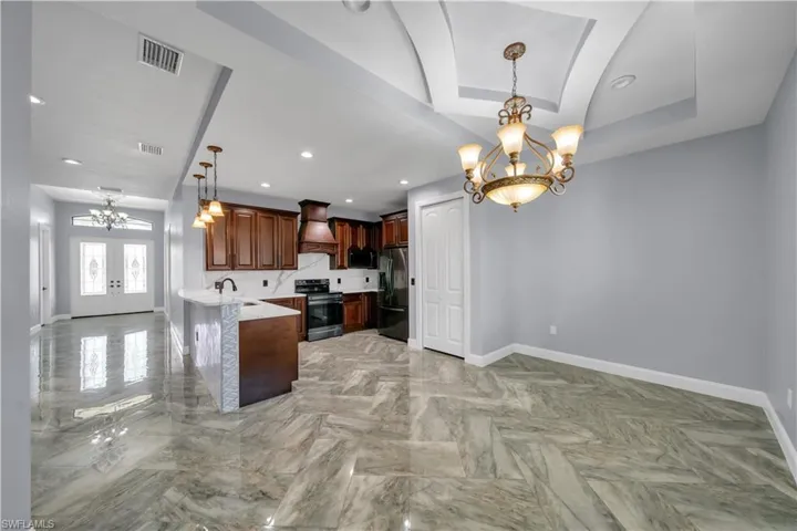 Kitchen with custom exhaust hood, fridge with ice dispenser, black microwave, a notable chandelier, and stainless steel range with electric stovetop