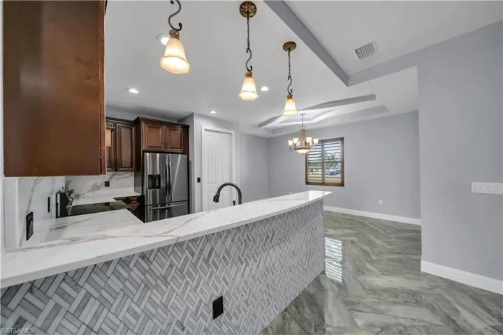 Kitchen featuring light stone countertops, stainless steel fridge, visible vents, a peninsula, and baseboards