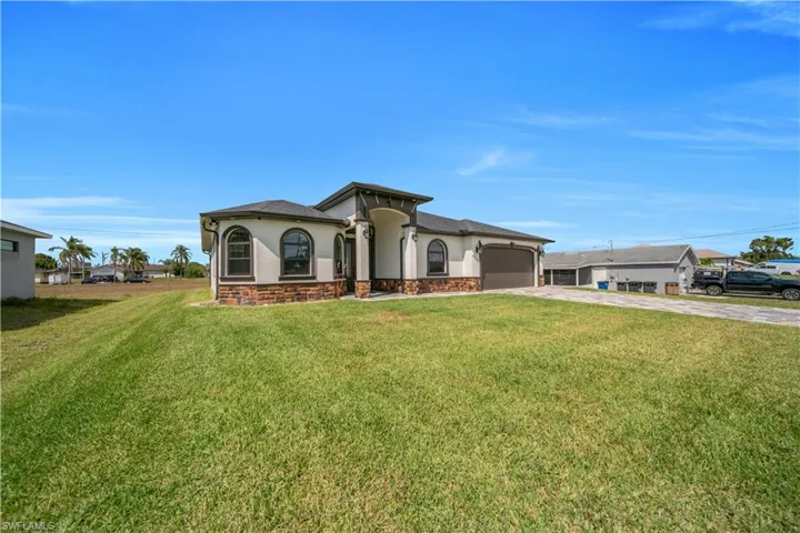 Mediterranean / spanish-style house with a garage, stucco siding, stone siding, a front lawn, and concrete driveway