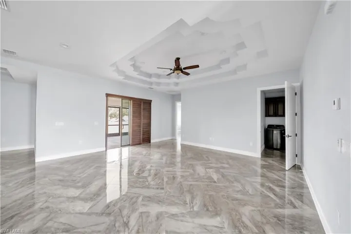Empty room featuring visible vents, ceiling fan, baseboards, and a raised ceiling