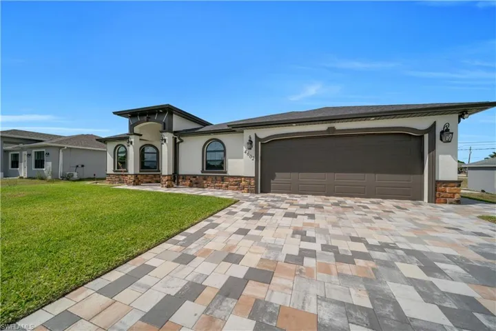 View of front facade featuring an attached garage, stone siding, stucco siding, a front lawn, and decorative driveway