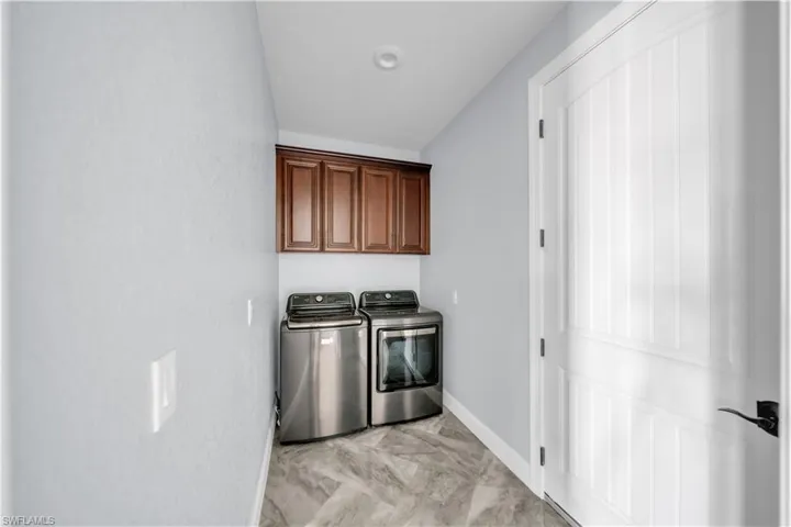 Laundry area featuring marble finish floor, washer and clothes dryer, baseboards, and cabinet space