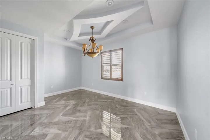 Unfurnished room featuring a tray ceiling, baseboards, and a chandelier