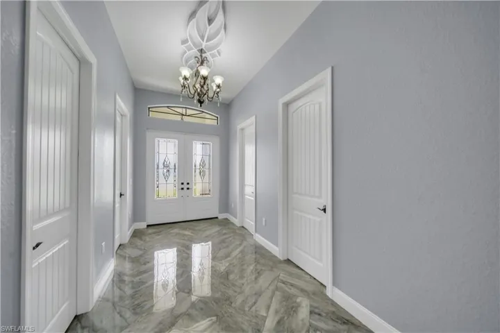 Entrance foyer with baseboards, an inviting chandelier, french doors, and marble finish floor
