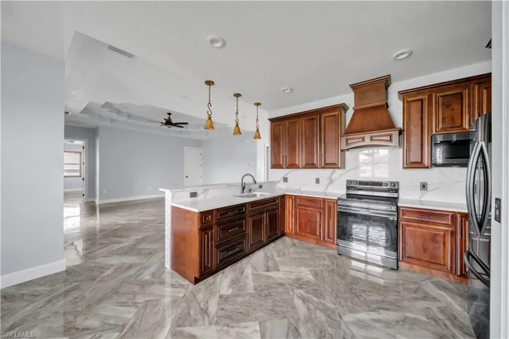 Kitchen featuring custom range hood, a peninsula, a tray ceiling, stainless steel appliances, and a sink