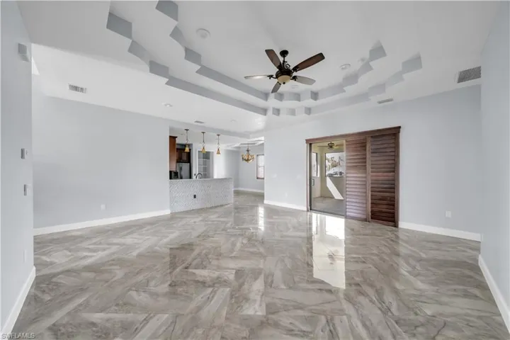Unfurnished living room with a tray ceiling, visible vents, ceiling fan with notable chandelier, and baseboards
