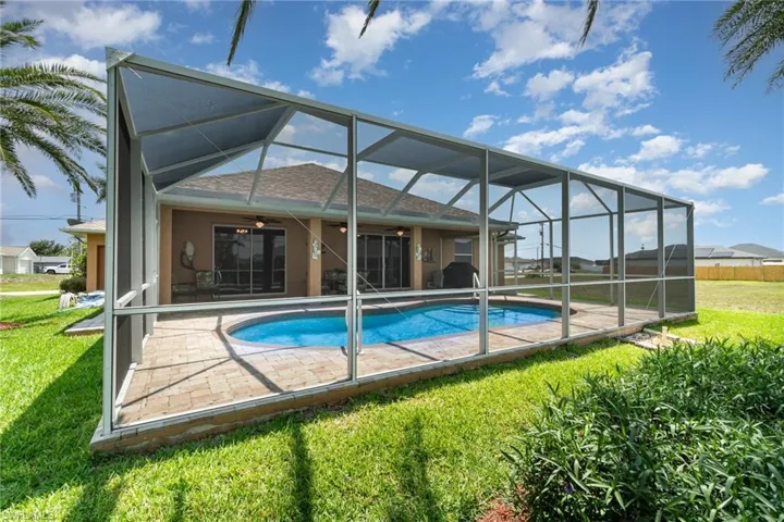 Rear view of house with ceiling fan, a yard, a patio, roof with shingles, and an outdoor pool