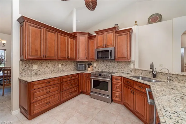 Kitchen with stainless steel appliances, a sink, vaulted ceiling, light tile patterned floors, and tasteful backsplash