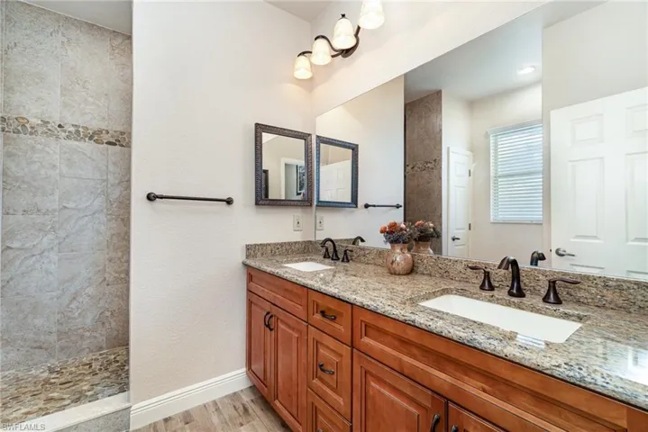 Full bath with wood finished floors, double vanity, walk in shower, and baseboards