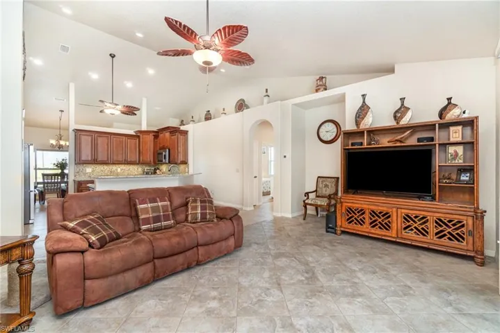 Living area with ceiling fan, arched walkways, lofted ceiling, baseboards, and a chandelier