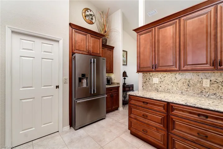 Kitchen with high end fridge, backsplash, light stone countertops, light tile patterned floors, and vaulted ceiling