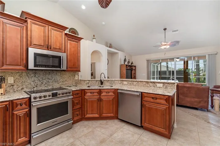 Kitchen featuring appliances with stainless steel finishes, vaulted ceiling, a sink, light tile patterned floors, and brown cabinets