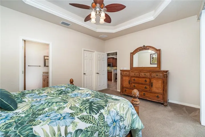 Bedroom featuring light colored carpet, ornamental molding, a tray ceiling, connected bathroom, and baseboards