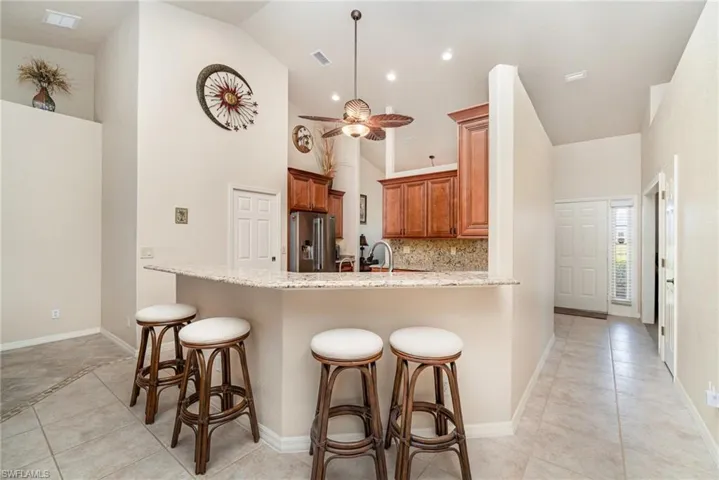 Kitchen with high end fridge, brown cabinetry, a peninsula, a kitchen bar, and high vaulted ceiling