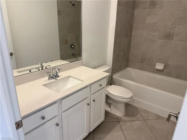 Bathroom 1 featuring a white vanity cabinet, a solid-surface countertop with an integrated basin, a full-width wall mirror, tile flooring, and a bathtub with a tile surround
