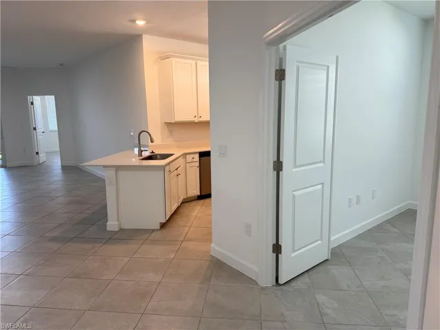 Kitchen and den featuring white cabinetry, solid-surface countertops, tile flooring, and a stainless steel dishwasher
