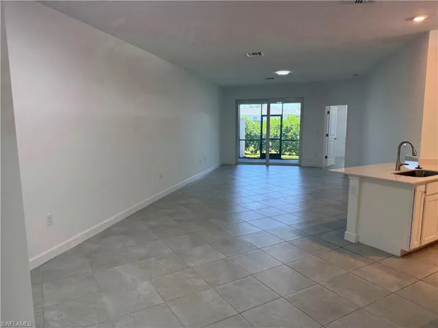 Open-concept interior featuring large-format tile flooring, recessed lighting, a center island with a quartz countertop, an undermount sink with a gooseneck faucet, and sliding glass doors leading to a screened enclosure