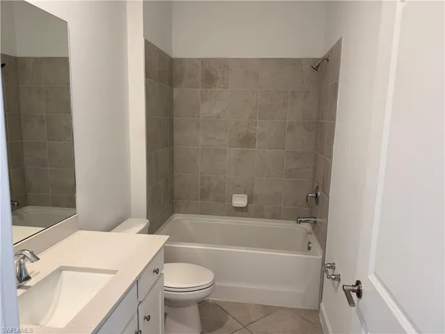 Bathroom 1 featuring a vanity with a light-toned countertop and integrated basin, a porcelain soaking tub with a tiled surround, and ceramic tile flooring