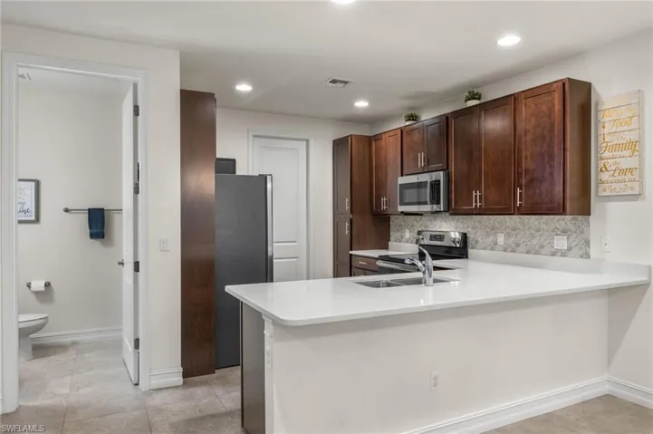 Kitchen featuring tasteful backsplash, light tile flooring, kitchen peninsula, and black & stainless appliances