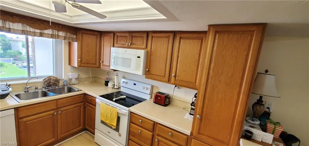 Kitchen featuring wood finish cabinets, white appliances, light countertops, and a ceiling fan