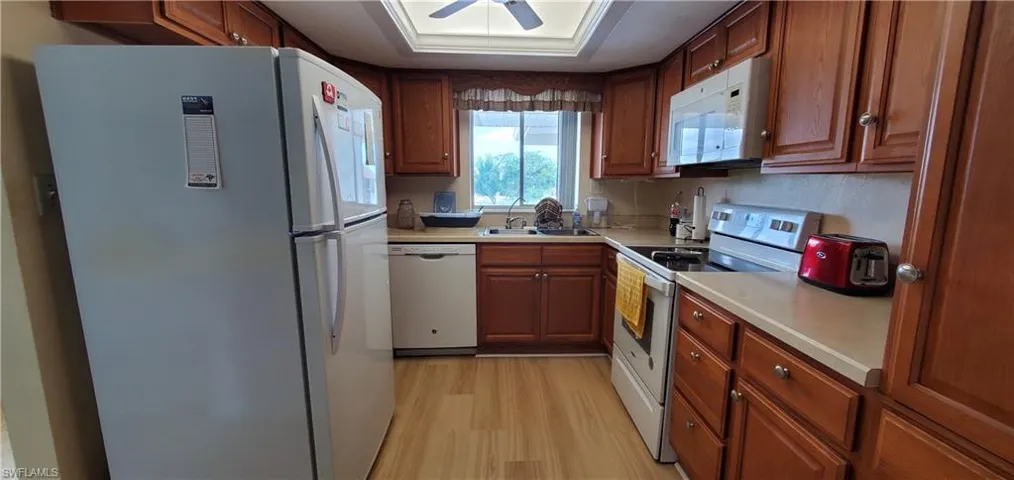 Kitchen featuring white appliances, wood finish cabinets, light countertops, and light wood finished floors