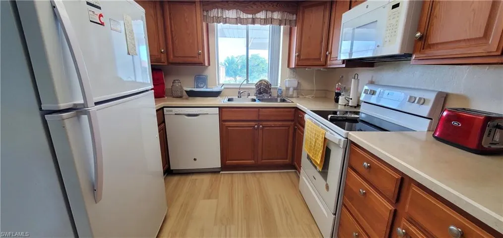 Kitchen with white appliances, wood finish cabinetry, light countertops, and light wood-style flooring