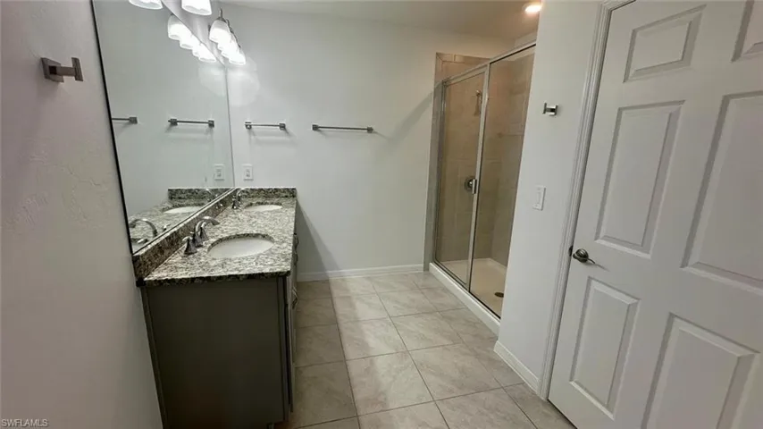 Bathroom featuring a shower stall, double vanity, and light tile patterned floors
