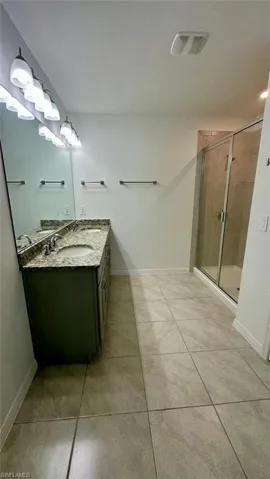 Bathroom featuring double vanity, a stall shower, and light tile patterned flooring