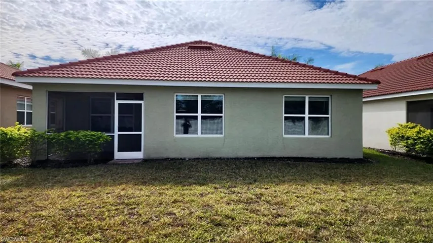 Back of property featuring stucco siding, a tile roof, a yard, and a sunroom
