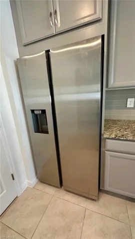 Kitchen view of light stone countertops, stainless steel refrigerator with ice dispenser, and backsplash