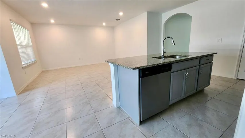 Kitchen with a center island with sink, dark stone countertops, dishwasher, arched walkways, and light tile patterned floors