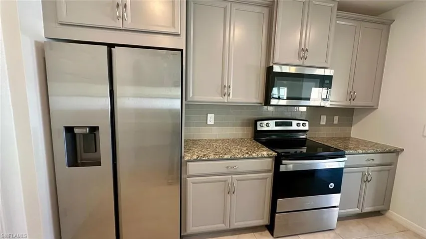 Kitchen featuring appliances with stainless steel finishes, gray cabinetry, light stone countertops, and tasteful backsplash