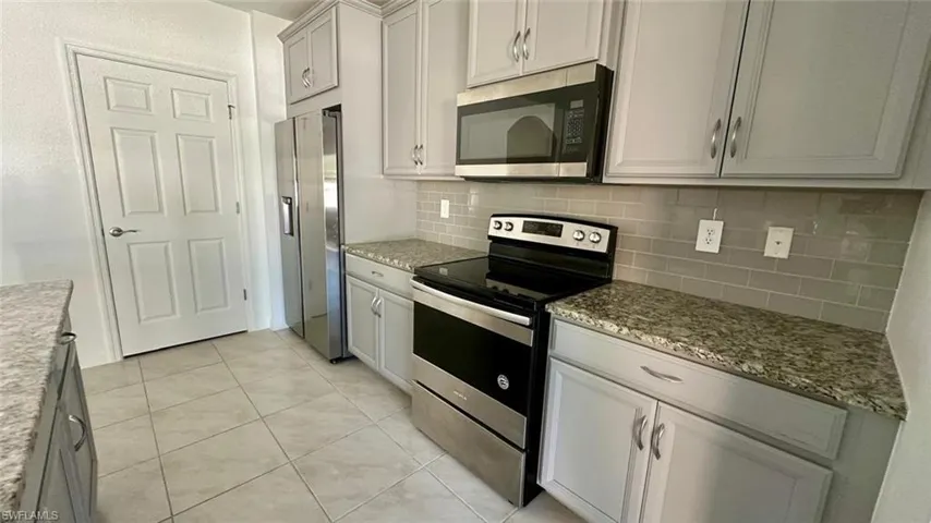Kitchen with stainless steel appliances, dark stone counters, light tile patterned floors, and tasteful backsplash