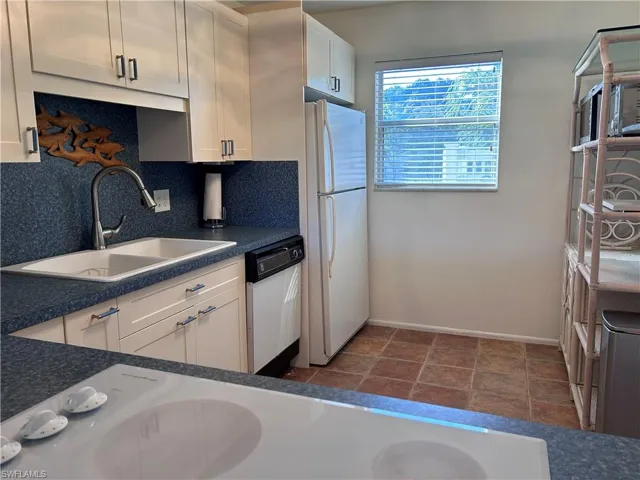 Kitchen with white cabinets, sink, backsplash, and white appliances
