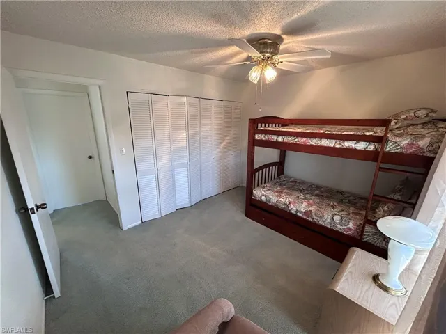 Carpeted bedroom with ceiling fan, a closet, and a textured ceiling