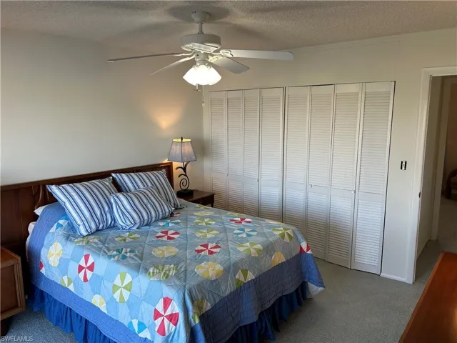 Carpeted bedroom featuring ceiling fan, a closet, and a textured ceiling