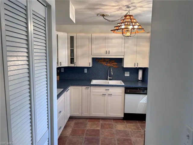 Kitchen featuring sink, tasteful backsplash, hanging light fixtures, dishwasher, and white cabinets