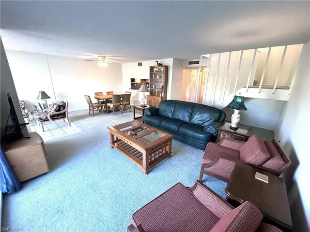 Carpeted living room featuring ceiling fan and a textured ceiling
