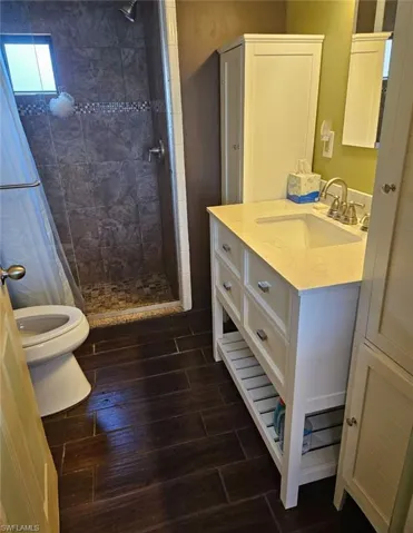 Bathroom with toilet, vanity, laminate flooring, and a tile shower
