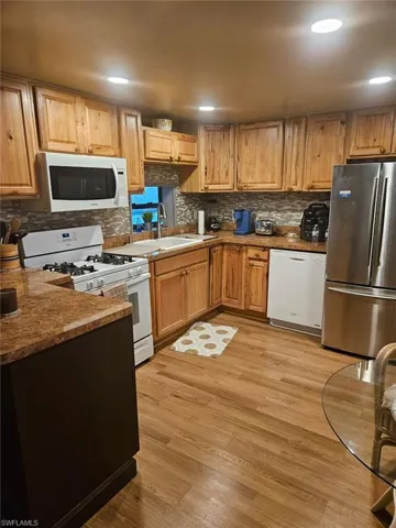 Kitchen featuring white appliances, sink, light laminate flooring, and decorative backsplash