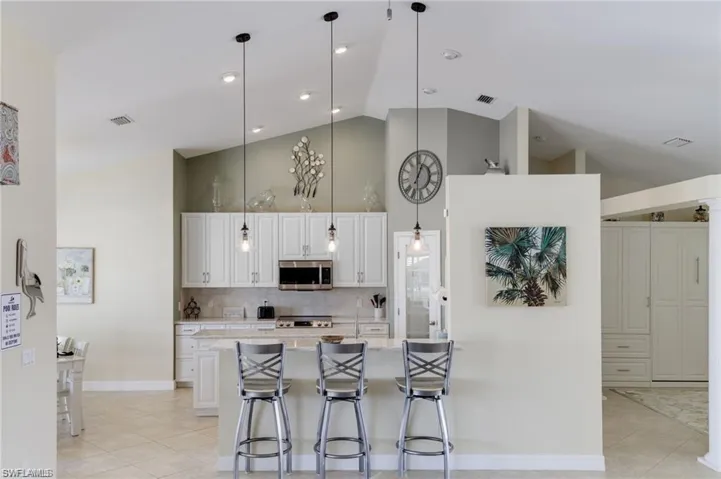 Kitchen with hanging light fixtures, decorative backsplash, light tile patterned floors, appliances with stainless steel finishes, and high vaulted ceiling