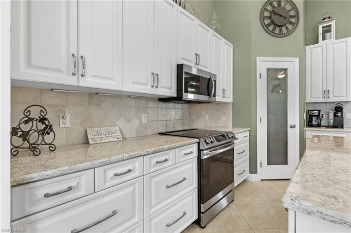 Kitchen featuring appliances with stainless steel finishes, white cabinetry, light stone counters, and decorative backsplash