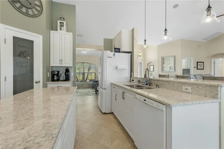 Kitchen with light stone countertops, arched walkways, white appliances, decorative light fixtures, and a peninsula