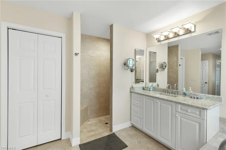 Bathroom featuring a closet, vanity, a shower stall, and light tile patterned floors