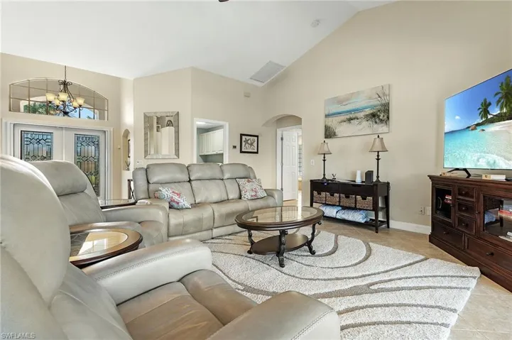 Living area featuring high vaulted ceiling, arched walkways, a chandelier, light tile patterned floors, and french doors