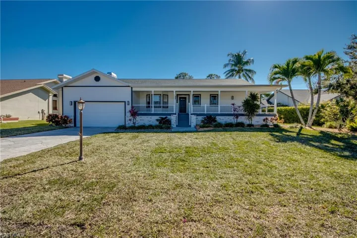 Single story home with a porch, a front lawn, driveway, and an attached garage