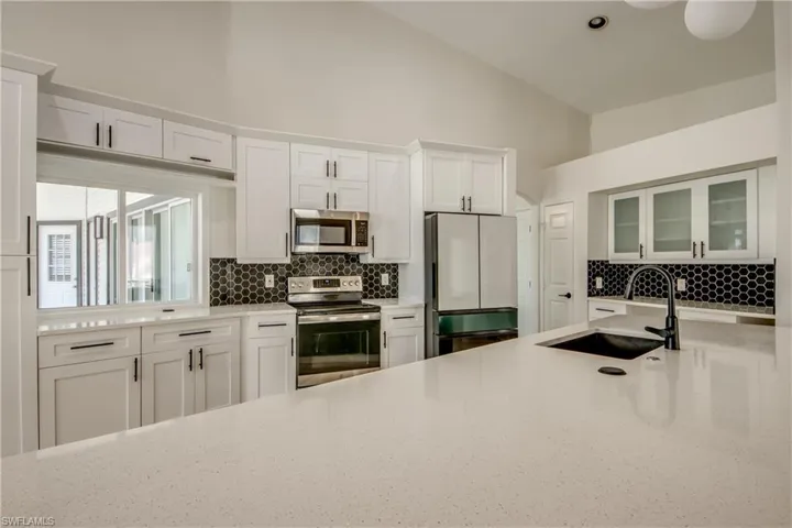 Kitchen with stainless steel appliances, white cabinetry, decorative backsplash, and high vaulted ceiling