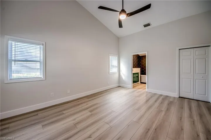 Unfurnished bedroom with high vaulted ceiling, light wood-style floors, a ceiling fan, a closet, and ensuite bath