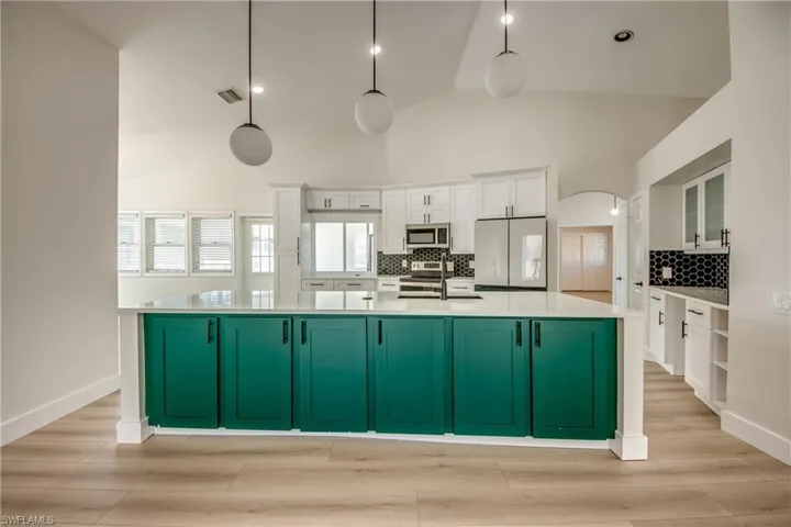 Kitchen with green cabinetry, white cabinetry, a large island, backsplash, and arched walkways